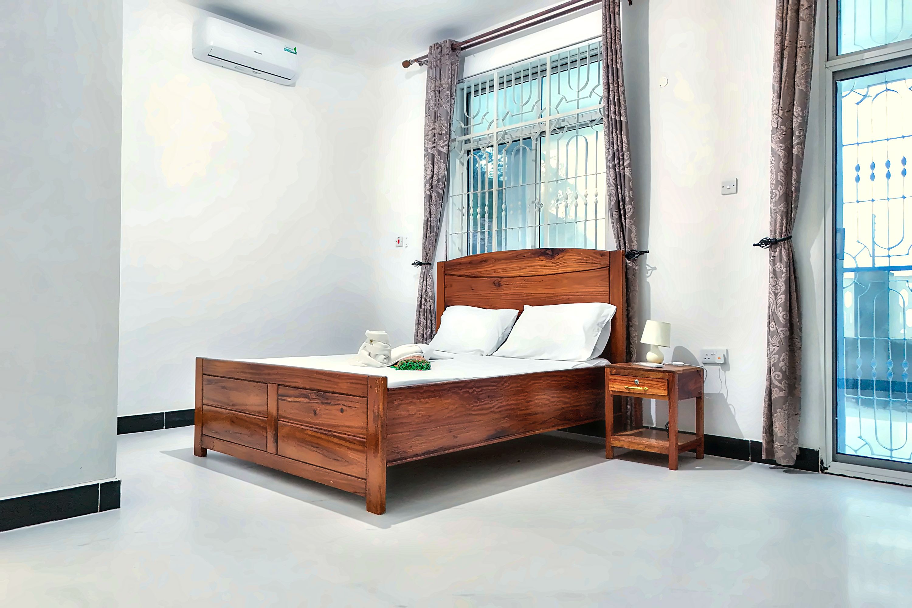 Un dormitorio con una cama de madera, una mesita de noche, una lámpara y una ventana con cortinas.