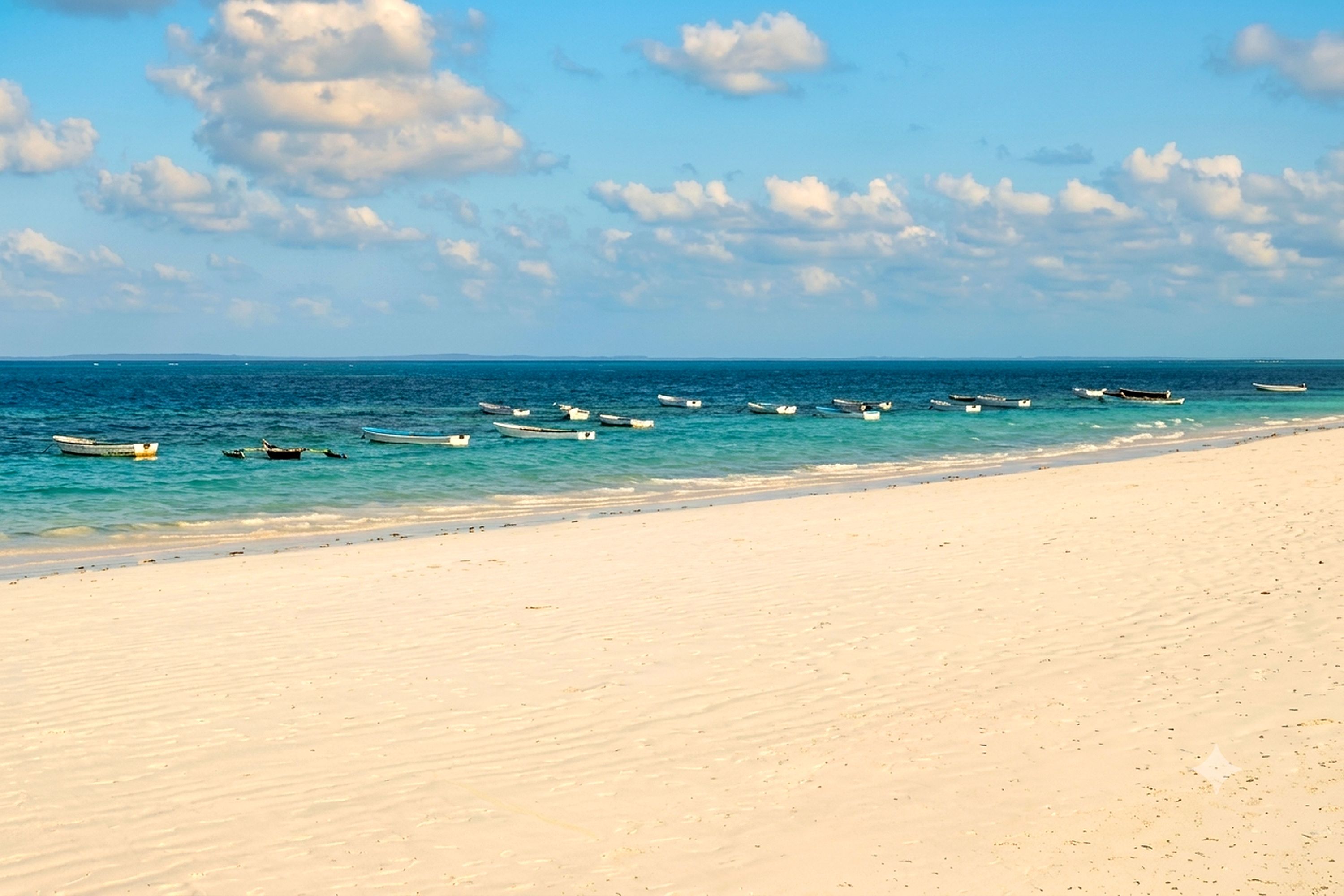 Una playa con barcos anclados en el agua y una orilla arenosa.