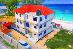 A multi-story building with a red roof, located near a beach with clear blue water. - Exclusive Beachfront Apartment in Uroa, Zanzibar - Ocean Views (Zanzibar, Uroa)