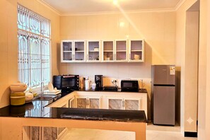 A kitchen with a black countertop, white cabinets, a stainless steel refrigerator, and a window with decorative bars. - Exclusive Beachfront Apartment in Uroa, Zanzibar - Ocean Views (Zanzibar, Uroa)