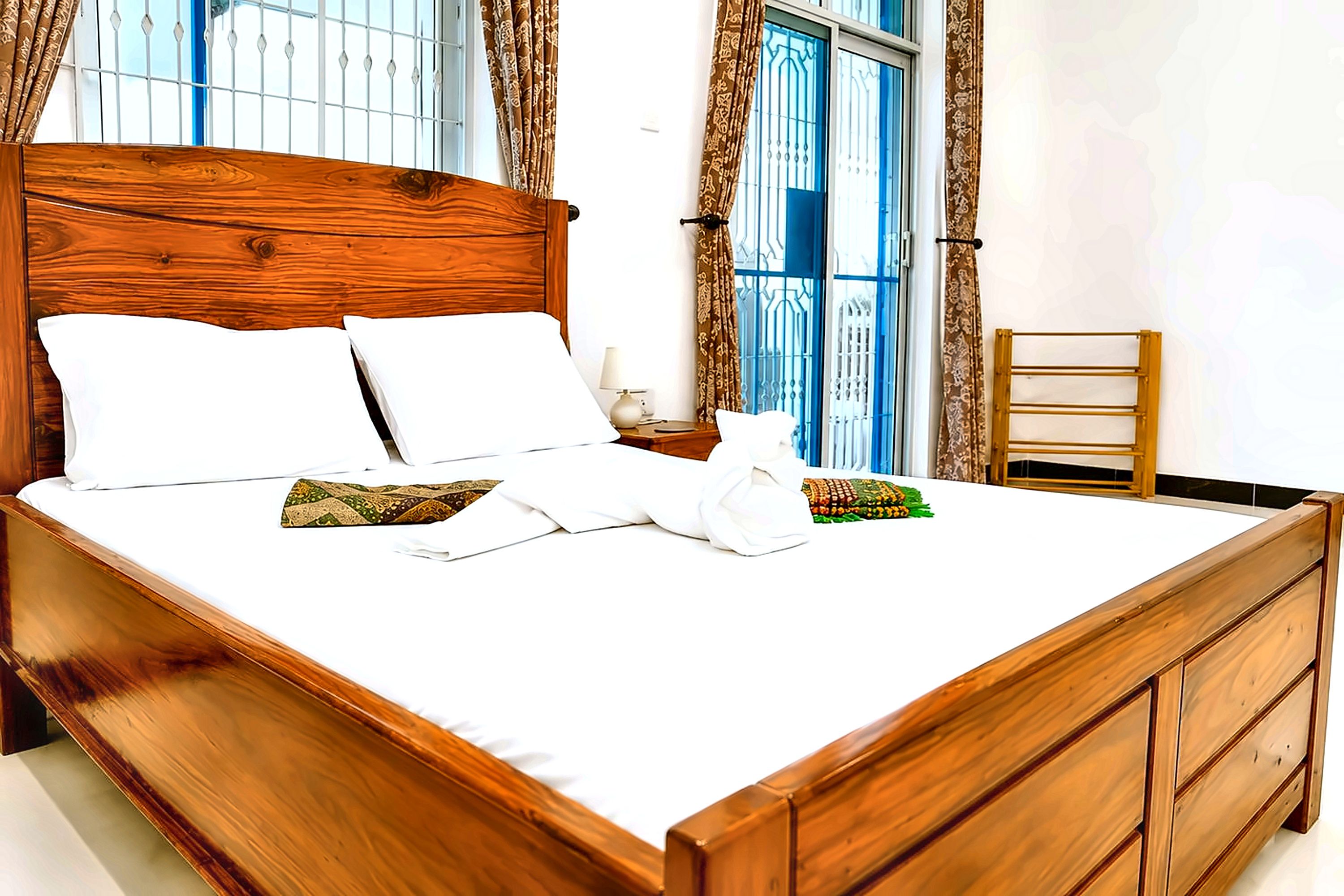 A neatly made bed with white linens and pillows, a wooden headboard, and a nightstand with a lamp.