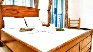 A neatly made bed with white linens and pillows, a wooden headboard, and a nightstand with a lamp.