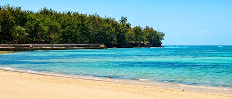 Una playa con agua turquesa cristalina, orilla de arena y una isla boscosa al fondo.