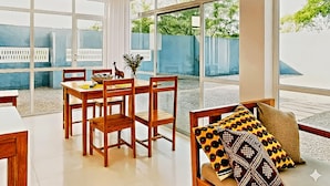 A dining area with a table and chairs, large windows, and a view of greenery outside. - Private Beachfront Apartment with Ocean Views in Zanzibar (Zanzibar, Uroa)