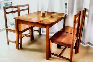 A wooden dining table with four chairs, a glass jar, and two placemats. - Serene Uroa Oceanfront Apartment (Zanzibar, Uroa)