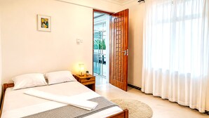 A bedroom with a bed, bedside table, lamp, and a view of a balcony through an open door. - Private Beachfront Apartment with Ocean Views in Zanzibar (Zanzibar, Uroa)