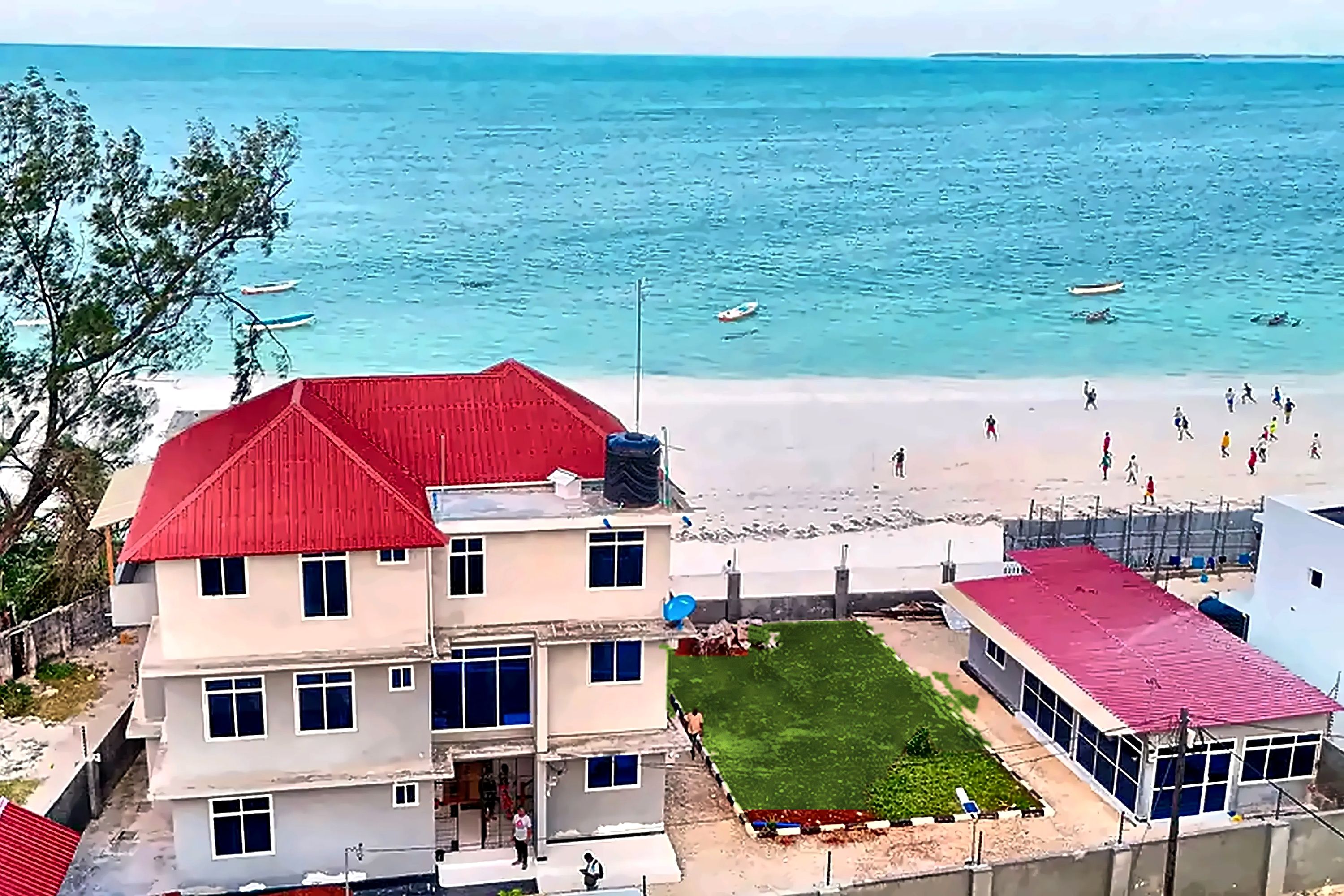 Une propriété située en bord de mer, avec un bâtiment à toit rouge, une pelouse et une vue sur l’océan.