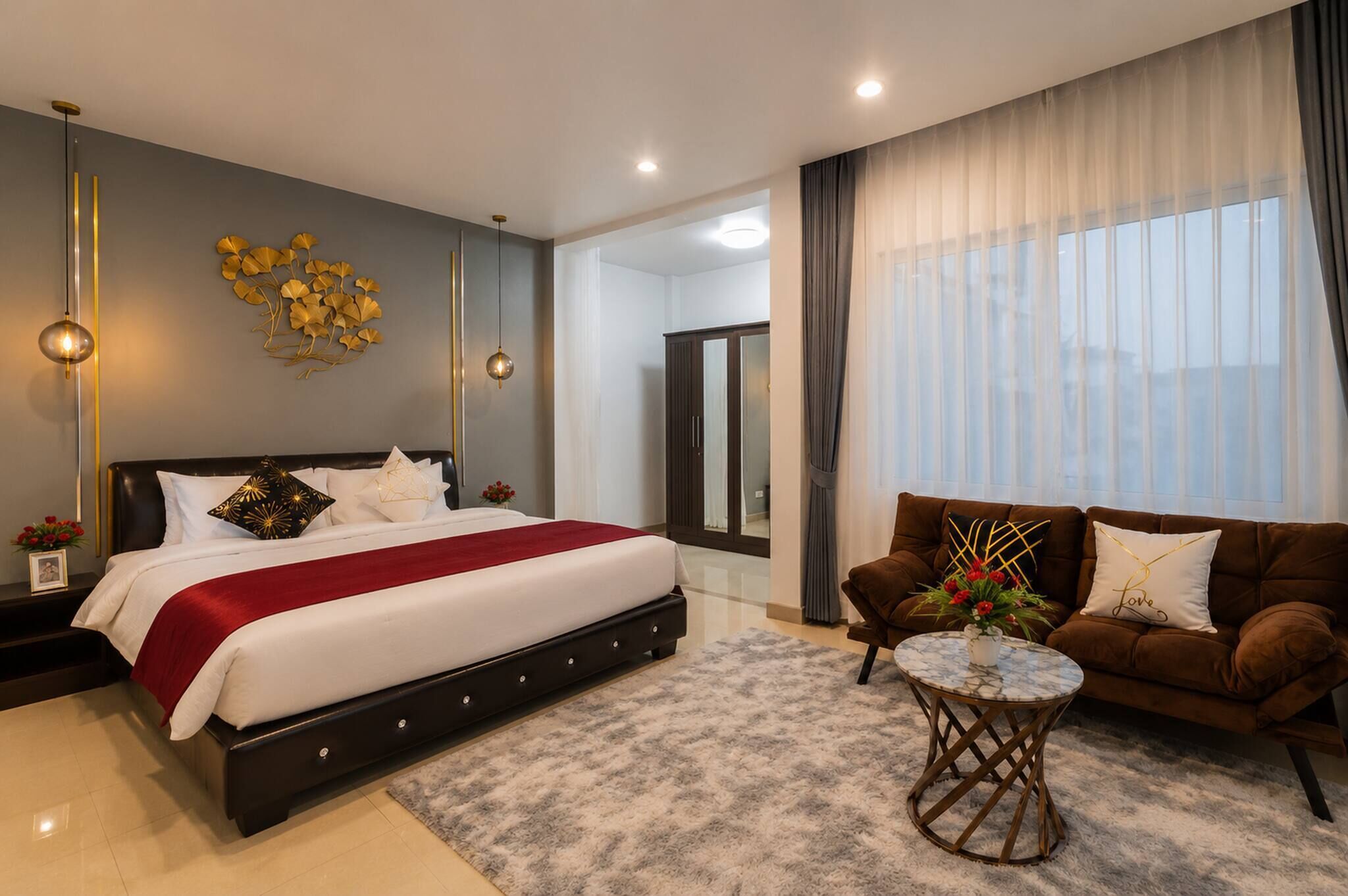 A modern bedroom with a large bed, a sofa, a small table, and a mirror.
