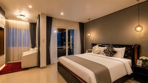 Moderni hotellihuone, jossa on suuri sänky, oleskelualue ja näkymä kaupunkiin.