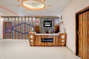Un mostrador de recepción con un letrero que dice 'Reception', una pared con rayas verticales y un plafón con una lámpara central.