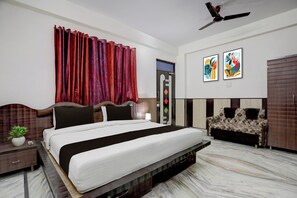 A bedroom with a bed, a nightstand, a potted plant, a ceiling fan, and two abstract paintings on the wall. - Super OYO Collection O Gautameshver (Varanasi)