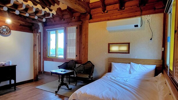 A wooden room with a bed, a desk, and a chair. - Hanok Pension Daega (Jeju City)