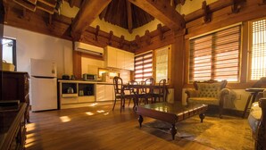 A spacious living area with a piano, wooden flooring, and a kitchen in the background. - Hanok Pension Daega (Jeju City)