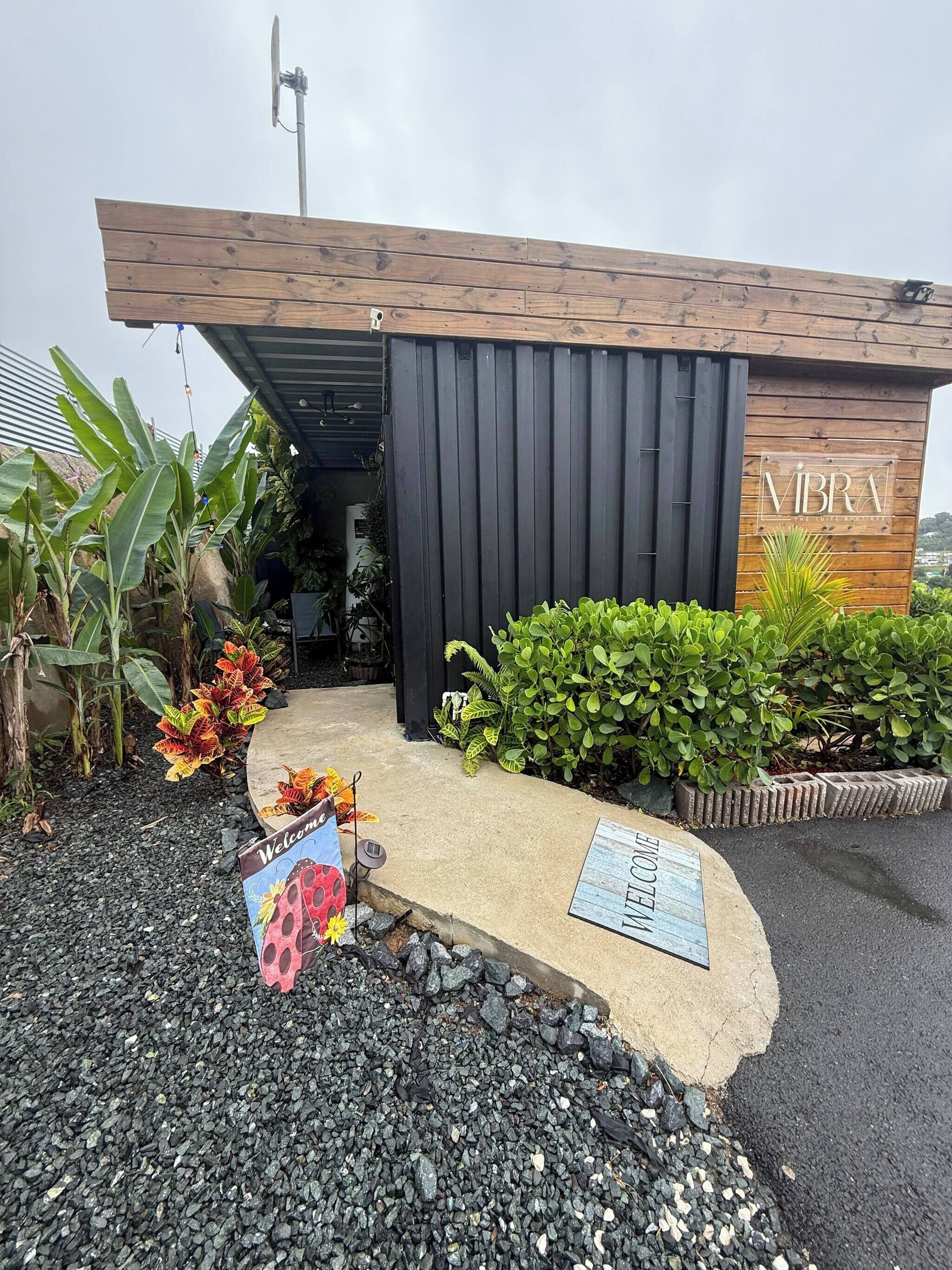 A modern building with a wooden facade and a black entrance door. There is a welcome mat and a sign with the name 'VIBRA' on the right.