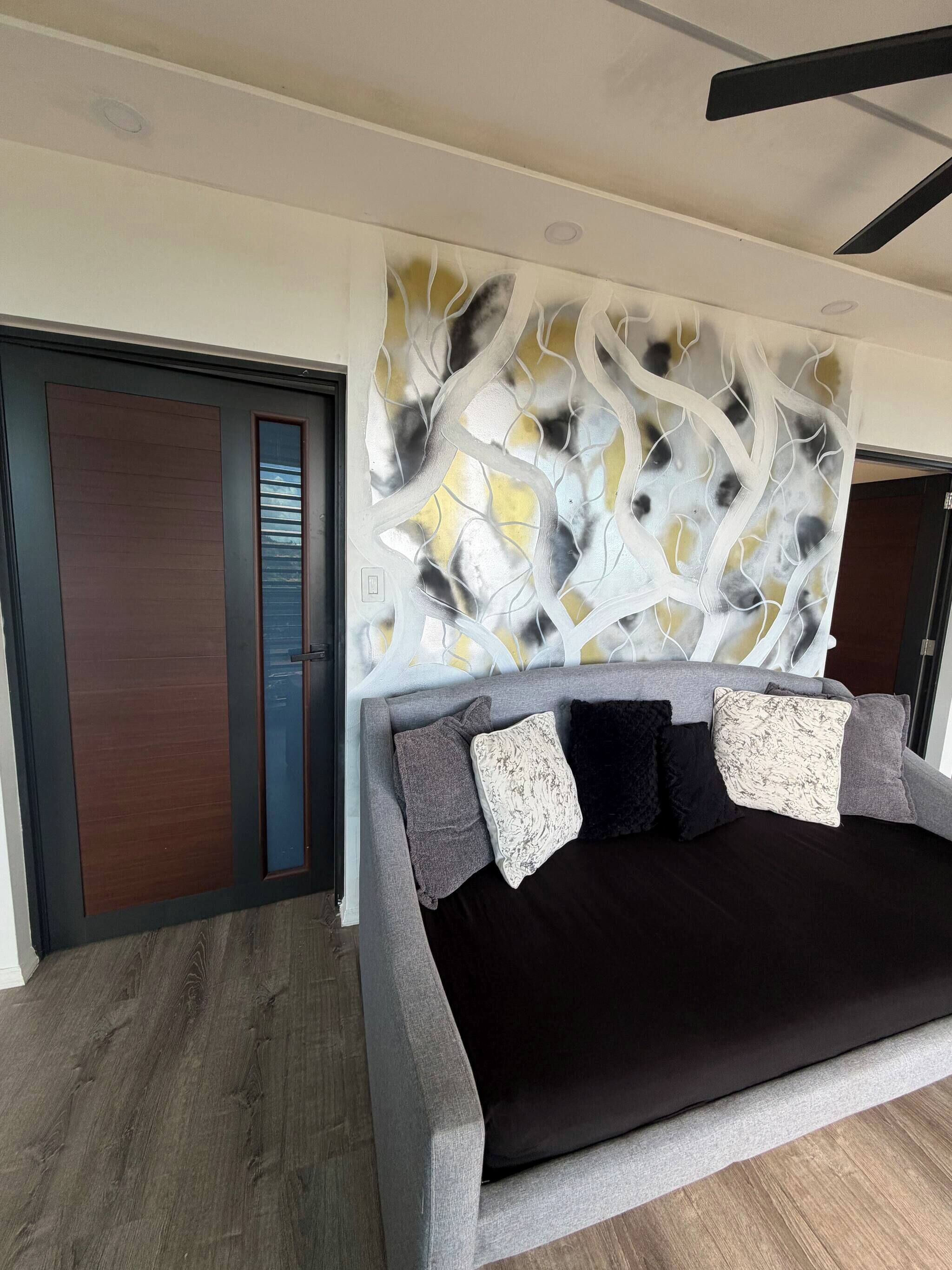 A modern bedroom with a grey sofa, dark cushions, and a decorative wall panel.