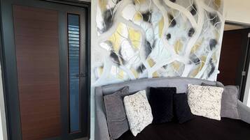 A modern bedroom with a grey sofa, dark cushions, and a decorative wall panel.