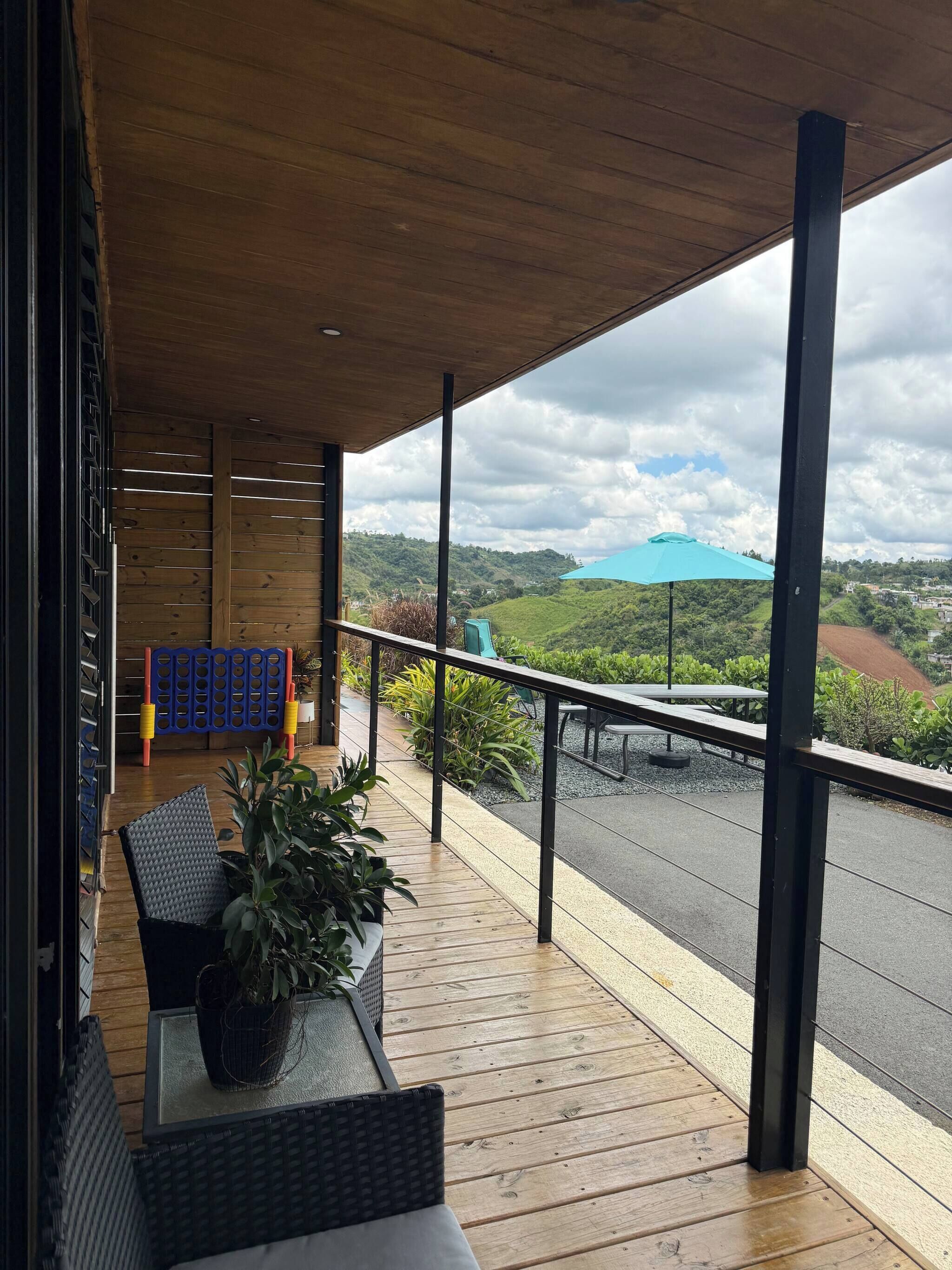 A wooden deck with outdoor furniture, a view of a green landscape, and a blue umbrella.