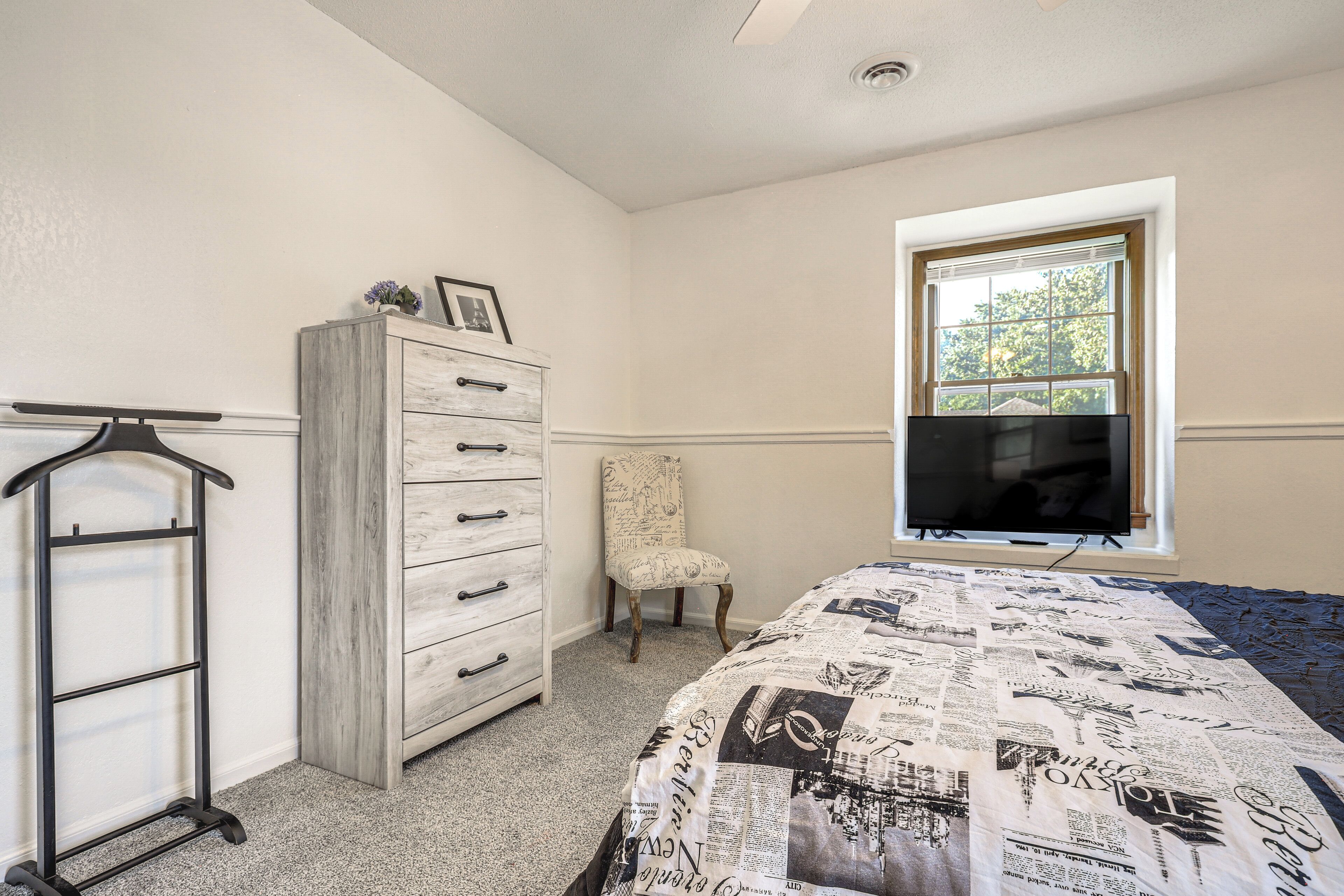 A bedroom with a bed, dresser, chair, and a window.