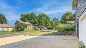 A residential street with houses, a driveway, and a clear sky. - Private Yard & Patio! Overland Park Group Getaway (Overland Park)