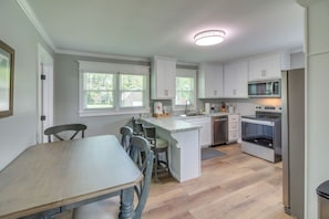 Una cocina moderna con armarios blancos, una isla central y una zona de comedor con mesa y sillas de madera.