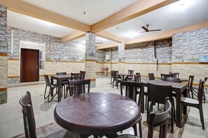 Uma ampla sala de jantar coberta, com paredes de pedra e ventiladores no teto.