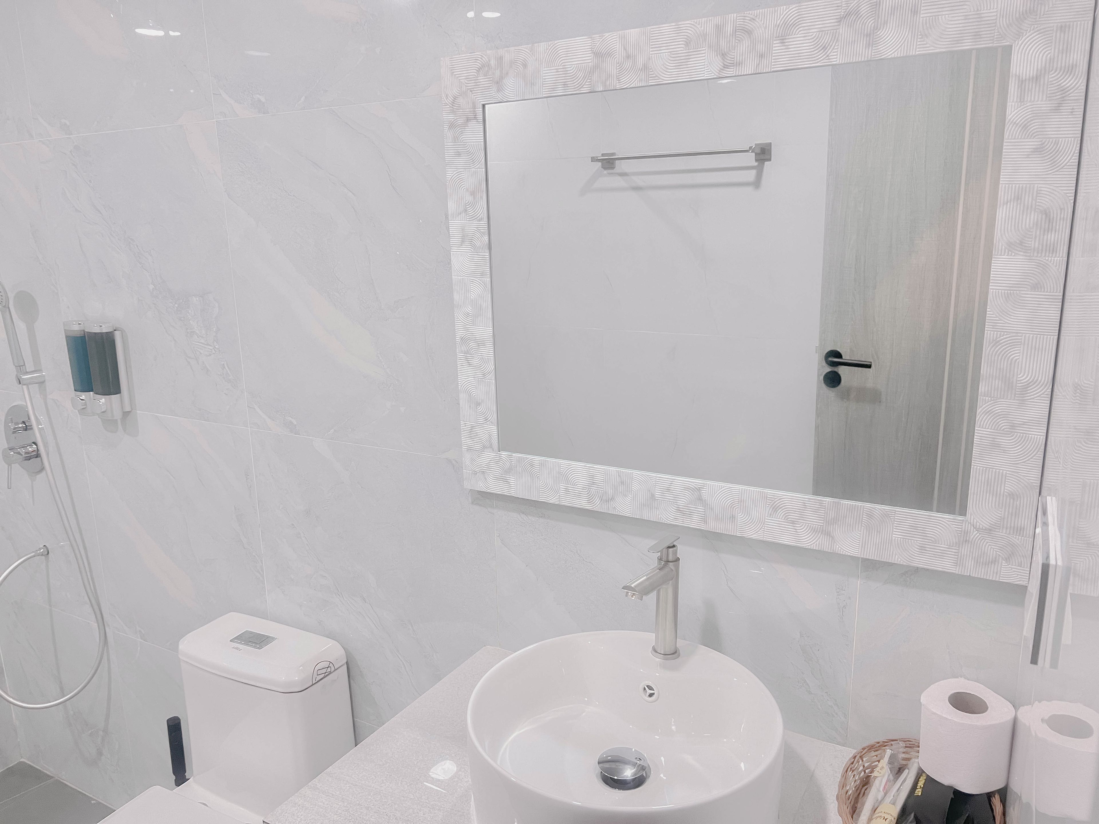 A modern bathroom with a white sink, a mirror with a decorative frame, a handheld showerhead, and a toilet.