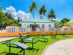 A building with a green roof, surrounded by palm trees and a colorful fence.
