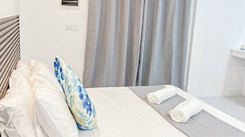 Habitación de hotel con cama, mesita de noche, lámpara, ventana con cortinas y aire acondicionado.