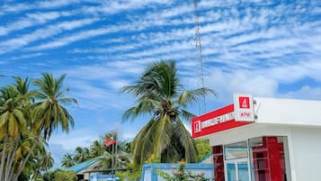 Un banco con un letrero rojo y blanco, palmeras y un cielo despejado.