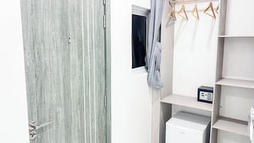 Una habitación con una puerta texturizada gris, una ventana con cortina, un perchero de madera y un mueble blanco para guardar objetos.