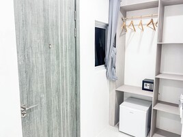 Una habitación con una puerta texturizada gris, una ventana con cortina, un perchero de madera y un mueble blanco para guardar objetos.