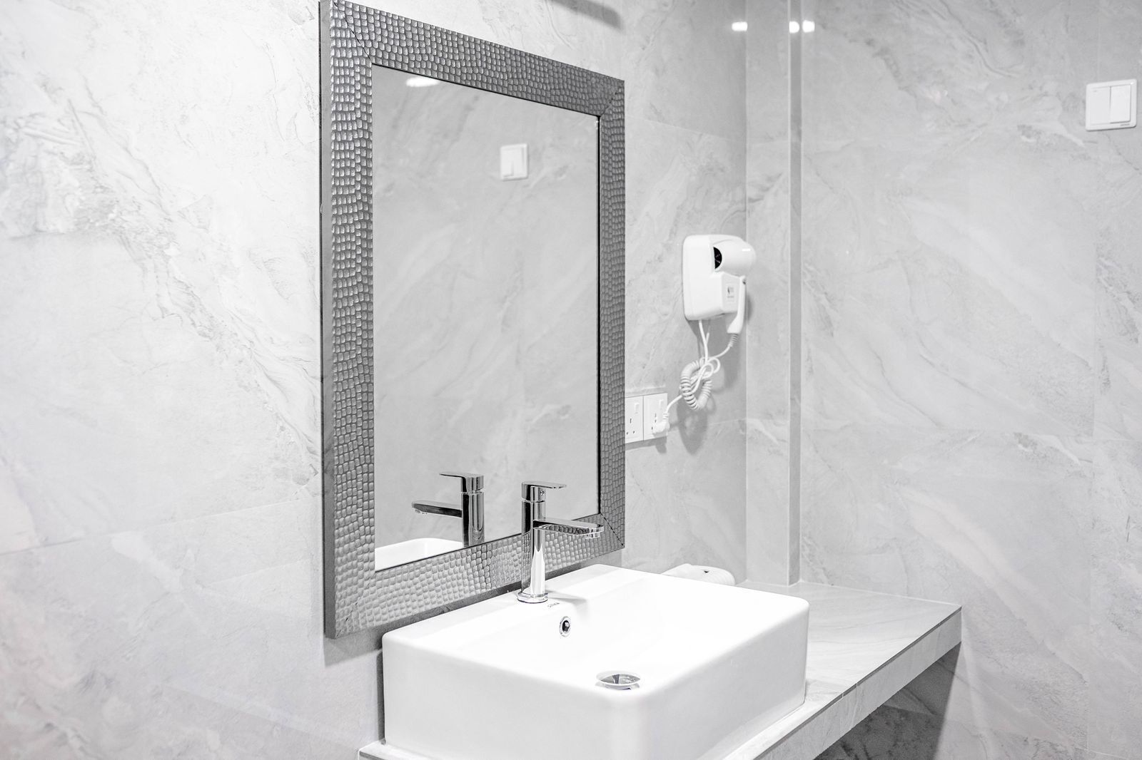 Un baño moderno con un espejo rectangular, un lavabo blanco y un secador de pelo de mano fijado a la pared.