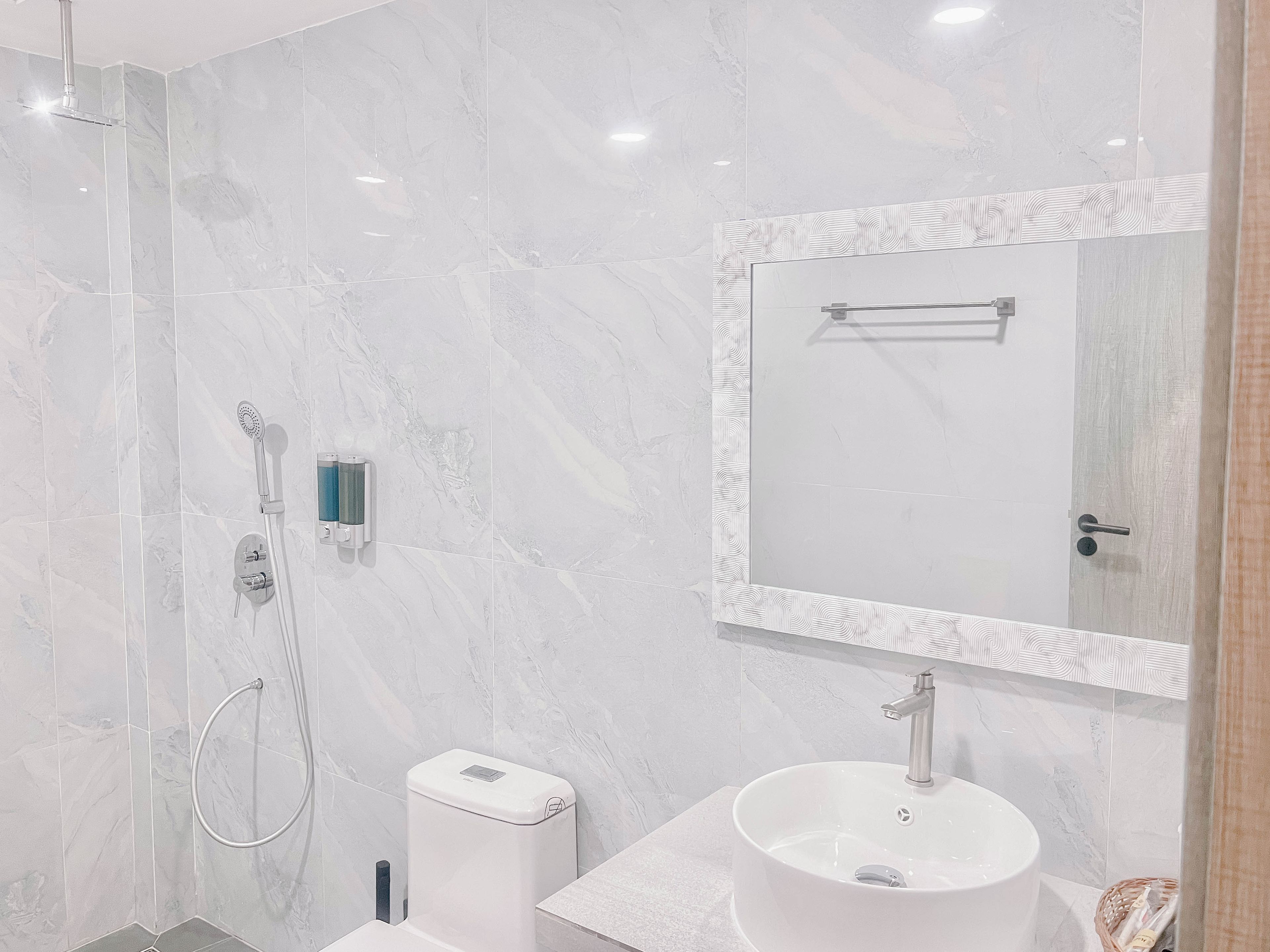 Un baño moderno con pared de mármol blanco, un espejo grande, un lavamanos y una ducha.
