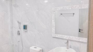 Un baño moderno con pared de mármol blanco, un espejo grande, un lavamanos y una ducha.