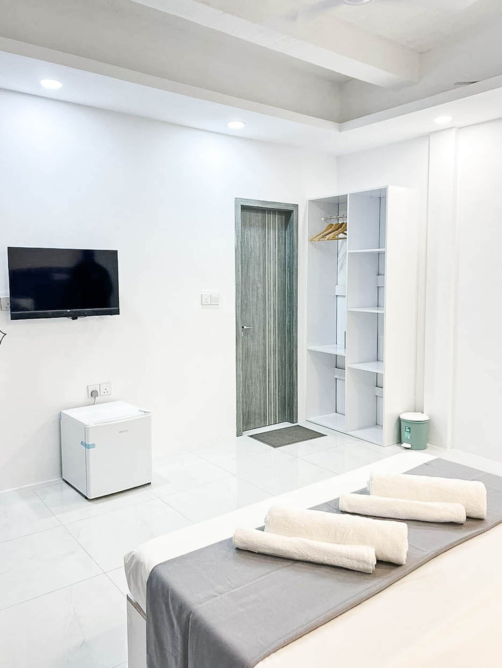 Una habitación de hotel moderna con una cama, televisión, mini refrigerador, armario y puerta.