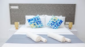 A hotel room with a bed, two pillows with a blue pattern, two bedside lamps, and two rolled towels on the bed. - Aquatic Mathiveri (Alifu Alifu Mathiveri)