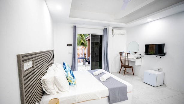 A hotel room with a bed, a desk, a chair, a TV, and an air conditioning unit. - Aquatic Mathiveri (Alifu Alifu Mathiveri)