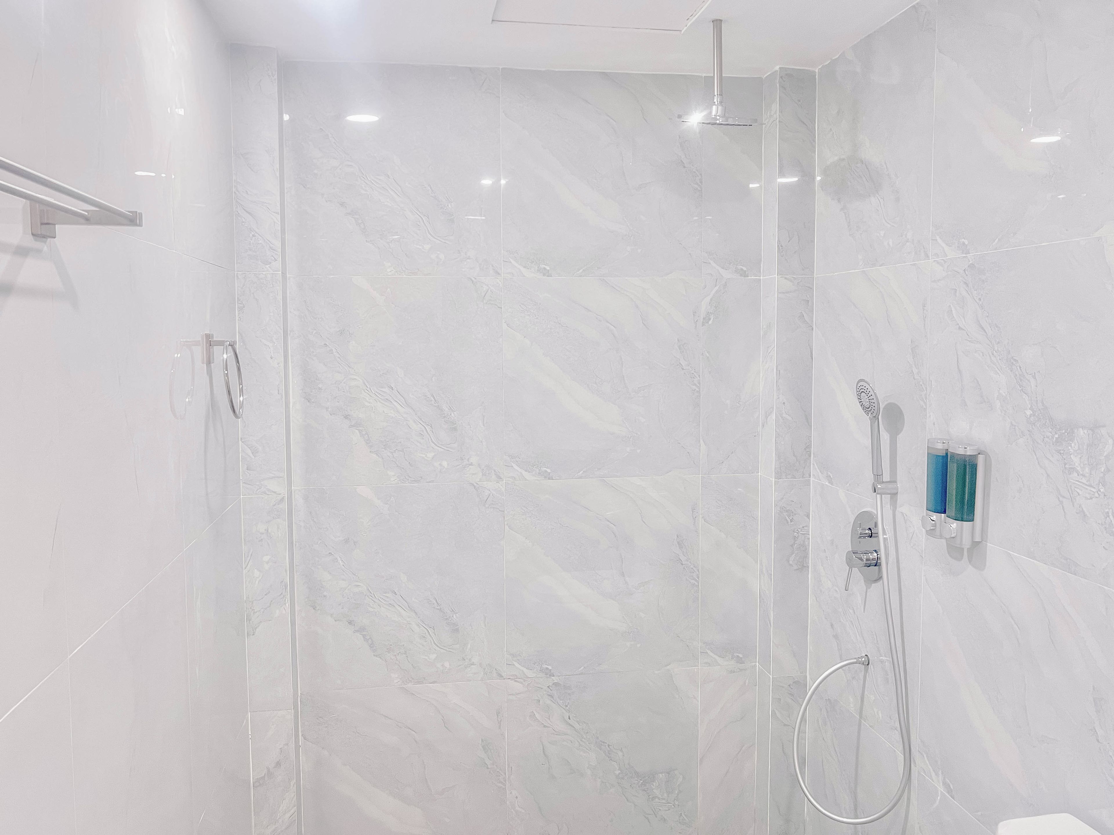 Un baño moderno con ducha envuelta en vidrio, cabezal de ducha manual y rociador de mano.