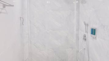 Un baño moderno con ducha envuelta en vidrio, cabezal de ducha manual y rociador de mano.