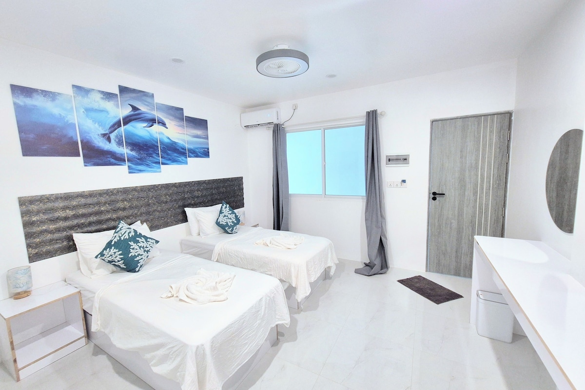 A hotel room with two beds, a desk, a window with curtains, and artwork on the wall.