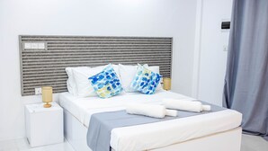 A neatly made bed with white bedding and blue patterned pillows, a bedside lamp, and a power outlet on the nightstand. - Aquatic Mathiveri (Alifu Alifu Mathiveri)