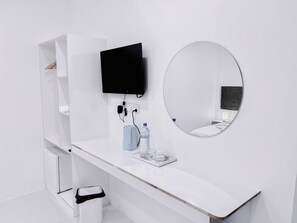 Un baño moderno con un tocador blanco, un espejo redondo, un televisor de pantalla plana y un pequeño cubo de basura.