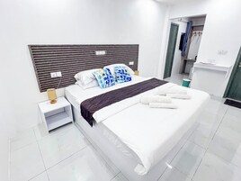 Una habitación de hotel moderna con una cama grande, una mesita de noche con lámpara y vistas al baño.