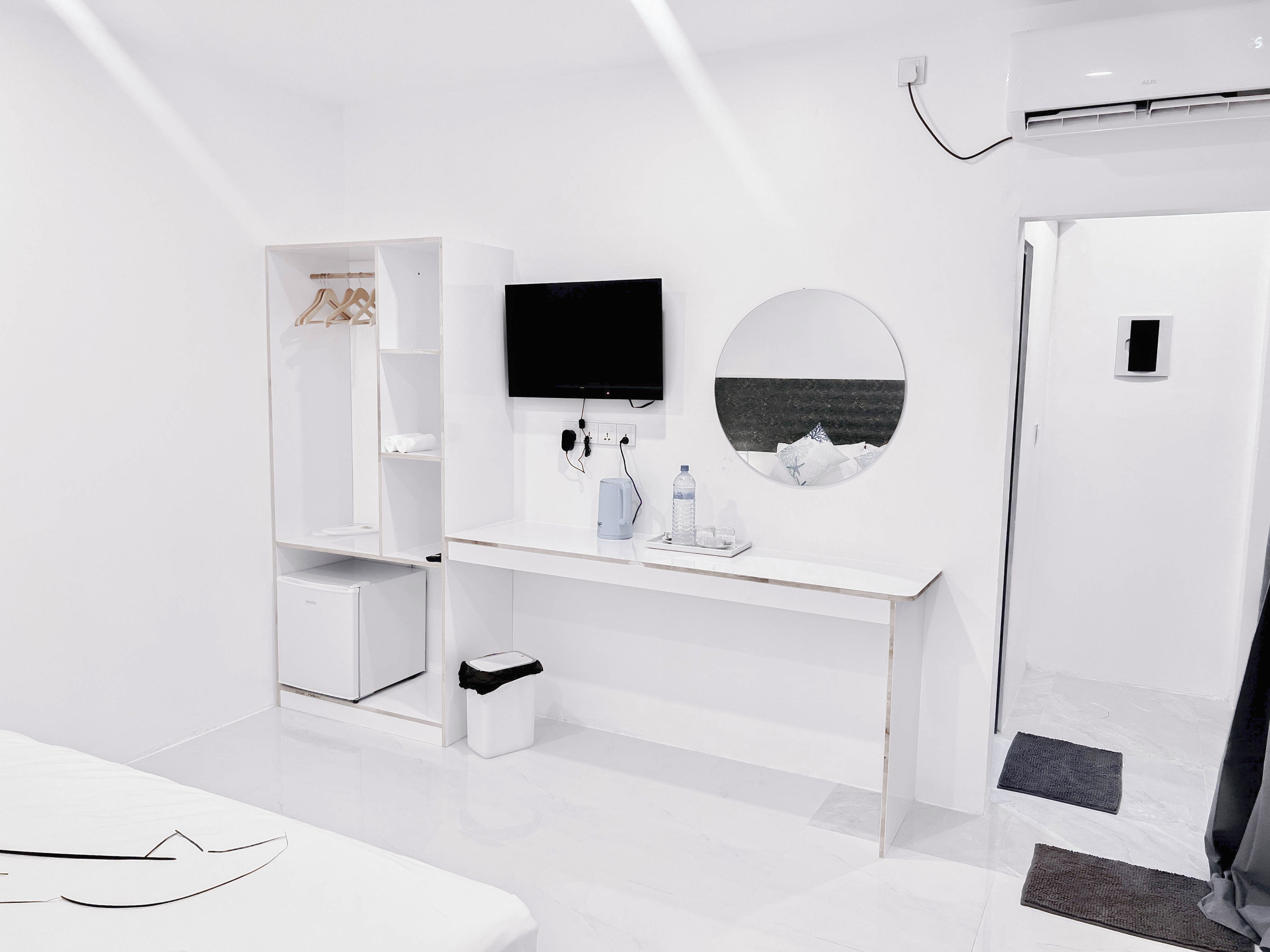 A modern hotel room with a white desk, a flat-screen TV, a round mirror, and a built-in wardrobe.
