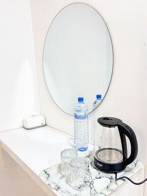Una encimera de baño con un espejo, un dispensador de pañuelos, dos botellas de agua, una jarra de vidrio y tres vasos.