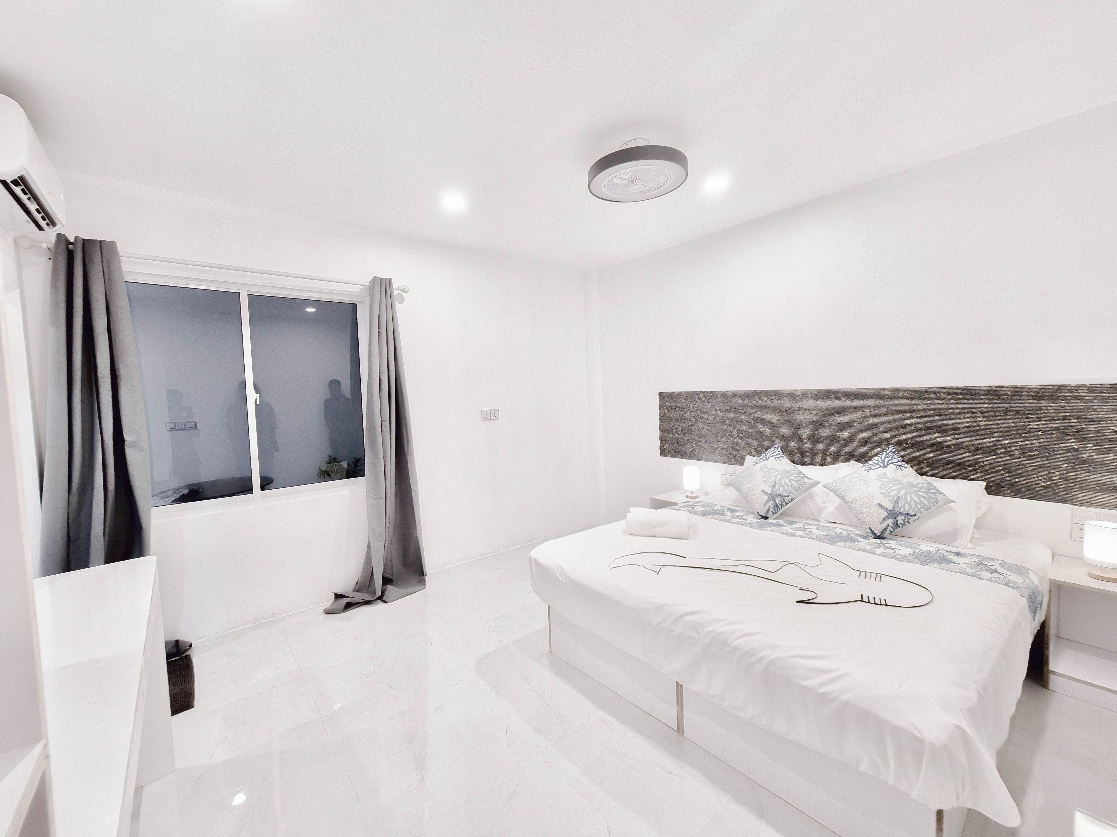 A modern hotel room with a large bed, a bedside table with a lamp, and a window with curtains.