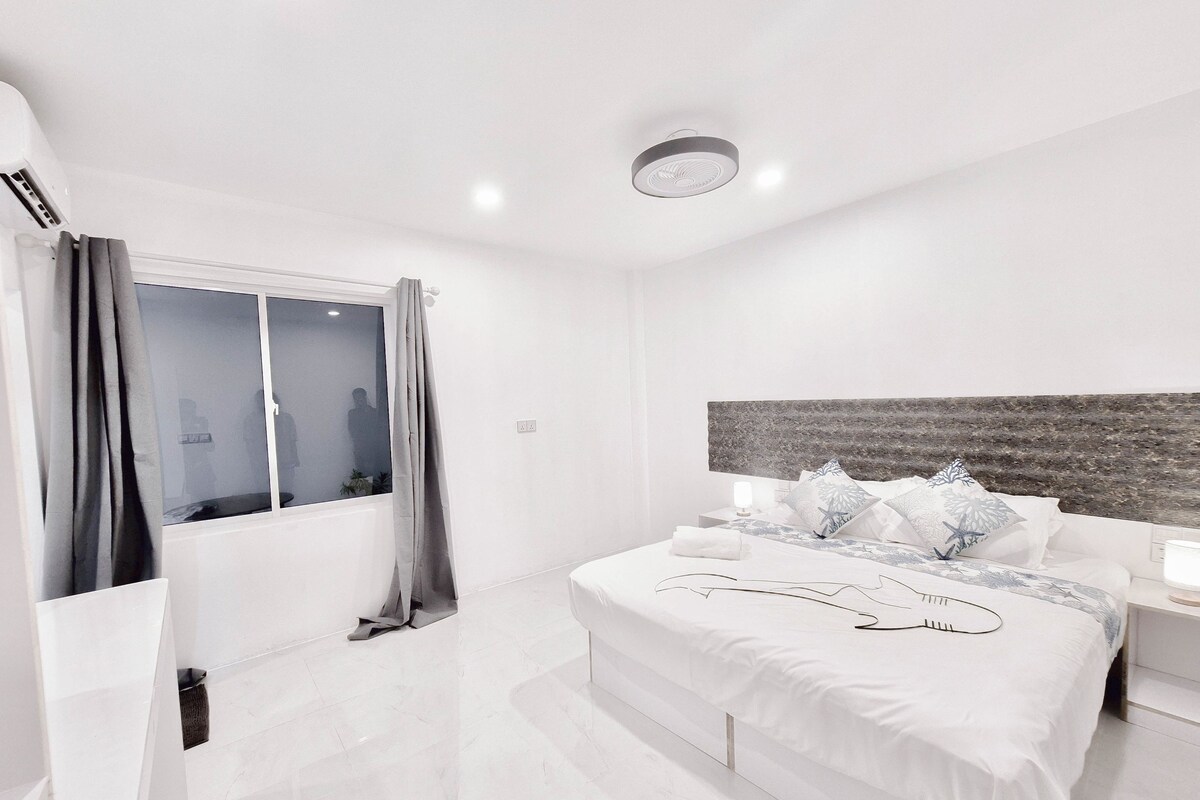 Une chambre d’hôtel moderne avec un grand lit, une table de chevet avec une lampe et une fenêtre avec des rideaux.