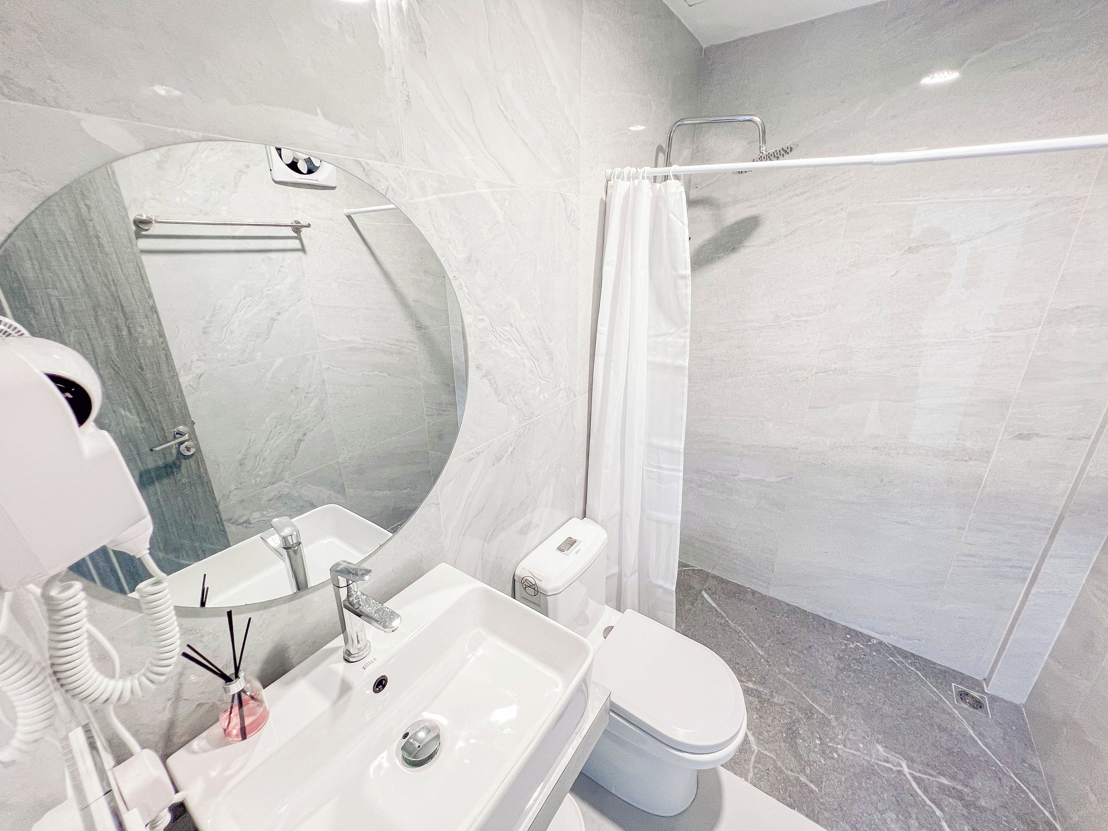 Un baño moderno con un espejo grande, un lavamanos, un inodoro y una zona de ducha.