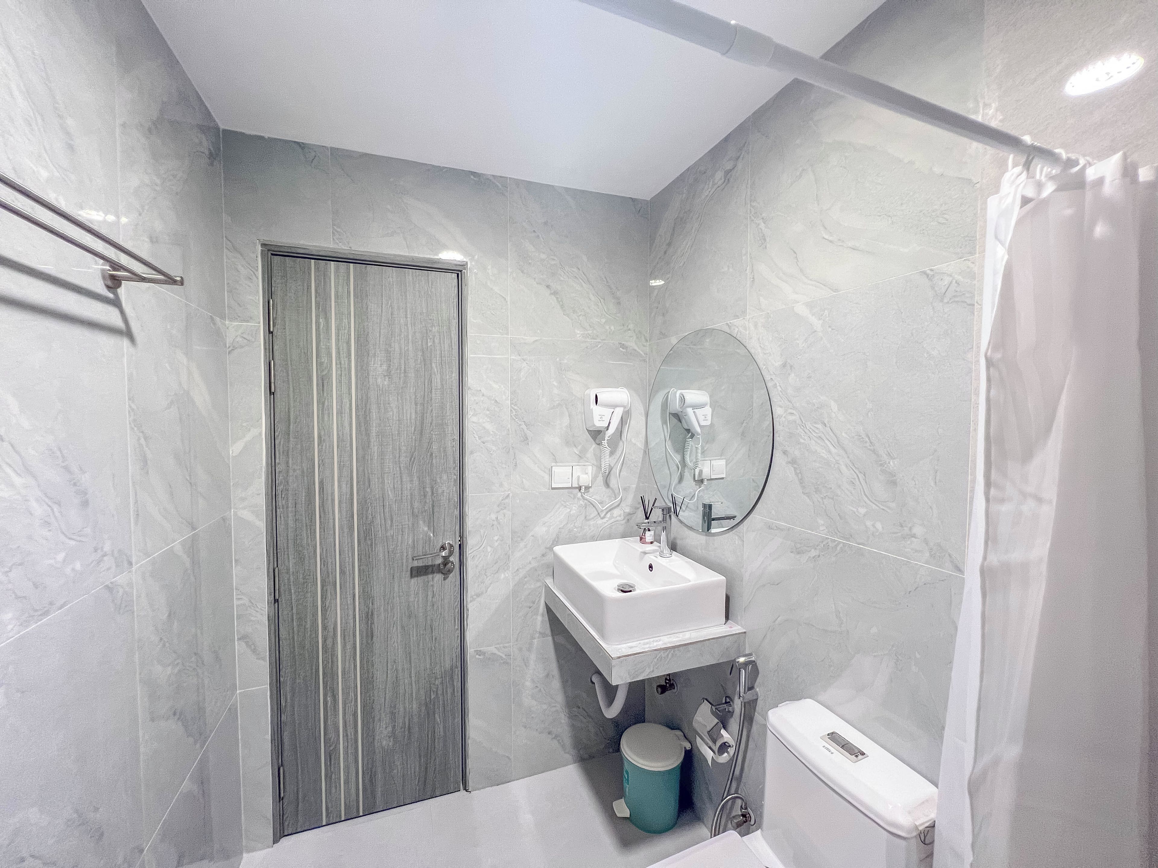 Un baño moderno con pared de mármol, un lavabo, un inodoro y una zona de ducha.