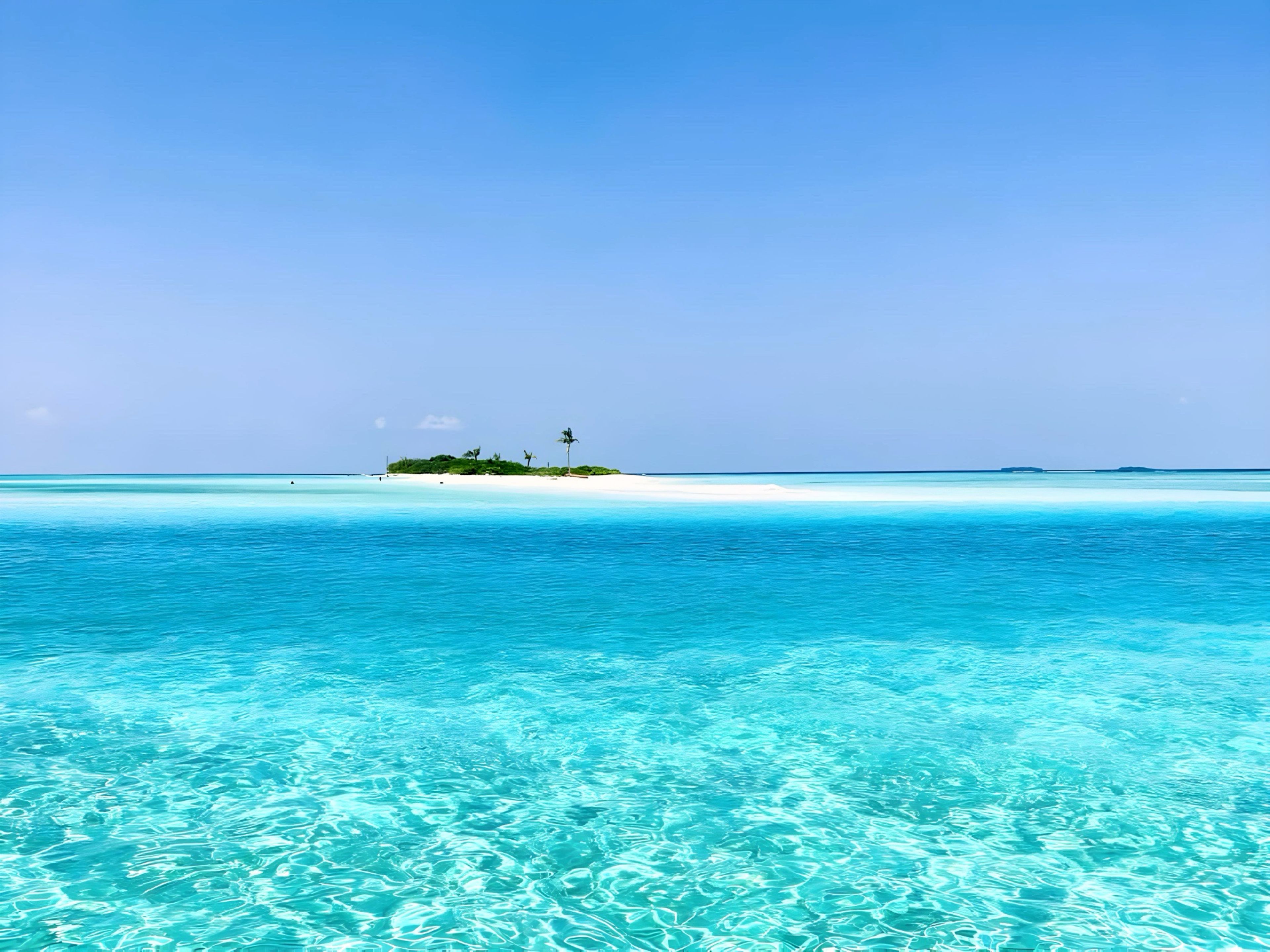 A tropical beach with clear turquoise water and a small island with vegetation.